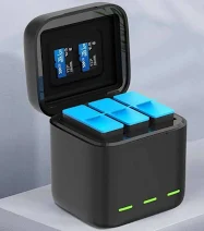 Three blue rechargeable batteries seated in a black charging dock with a hinged lid, green status LEDs on the front.